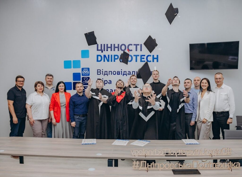 Випускники в мантіях підкидають академічні шапочки на тлі стіни з написом «Цінності Dniprotech»